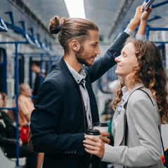 young couple with takeaway coffee standing in subway car.