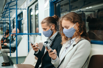 man and a woman with smartphones sitting in a subway car.