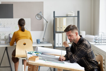 Fototapeta premium Side view portrait of mature bearded architect working on blueprints and plans while sitting at drawing desk in office, copy space
