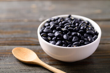 Black kidney beans in a bowl and spoon on wooden background