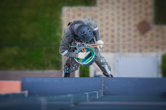 Professional climber rope access worker painting and repairing the facade of residential high rise building exterior facade wall, industrial mountaineer working at heights, risky job