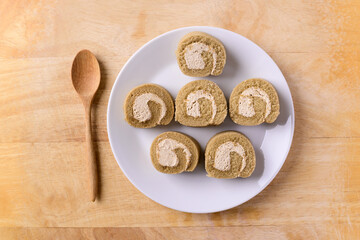 Coffee roll cake on white dish with spoon on wooden background, Top view