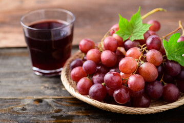 Fresh red grapes fruit in a basket and juice on wooden background
