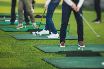 Obraz premium Group of golfers practicing and training golf swing on driving range practice, men playing on golf course, golf ball at golfing complex club resort