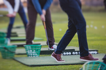 Obraz premium Group of golfers practicing and training golf swing on driving range practice, men playing on golf course, golf ball at golfing complex club resort
