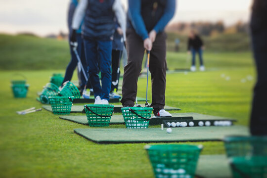 Group of golfers practicing and training golf swing on driving range practice, men playing on golf course, golf ball at golfing complex club resort