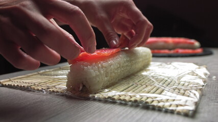 Cropped anonymous cook hands with rolling fresh sushi with bamboo mat while working in authentic Japanese restaurant,Close-up of chef's hands rolling a sushi roll on bamboo mat.Sushi making process