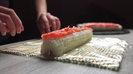 Cropped anonymous cook hands with rolling fresh sushi with bamboo mat while working in authentic Japanese restaurant,Close-up of chef's hands rolling a sushi roll on bamboo mat.Sushi making process