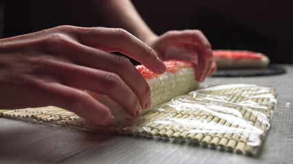 Obraz na płótnie Canvas Cropped anonymous cook hands with rolling fresh sushi with bamboo mat while working in authentic Japanese restaurant,Close-up of chef's hands rolling a sushi roll on bamboo mat.Sushi making process