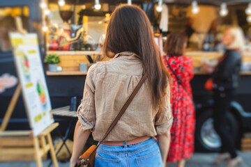 Girl ordering street food in colourful food truck van on food festival, summer sunny day