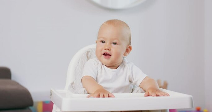 Portrait of smiling young baby in white high baby chair. White walls on background.
