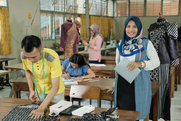 Muslim woman tailor in veiled standing with holding tablet pc beside the male tailor at the clothing production room