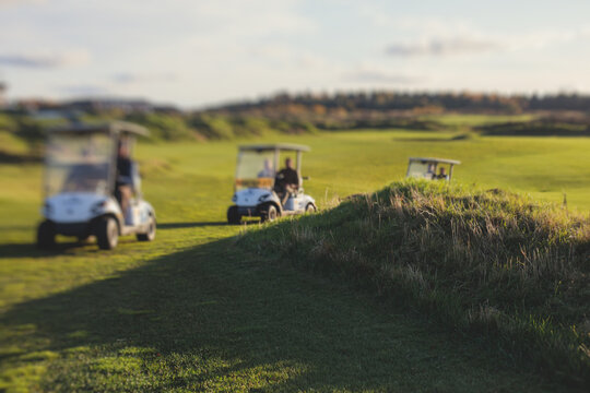 Golf electric cars riding on a golf course in the sunny day, golf carts drive with golfers in resort club