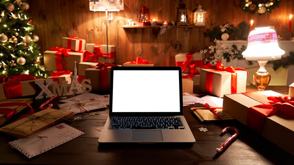Naklejka na ściany i meble Laptop computer with white blank empty mock up screen on Merry Christmas table with presents gifts, decorated Xmas tree in Santa house background. Ecommerce website online shopping delivery ads.