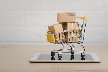 Brown paper boxs in  a shopping cart with tablet on wood table in office background.Easy shopping with finger tips for consumers.Online shopping and delivery service concept.