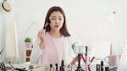 Young beautiful Asian woman professional beauty vlogger influencer recording make up tutorial video clip in bedroom at home for social media marketing