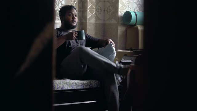 dark chubby guy having hot beverages on the couch watching tv