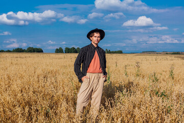Tall handsome man with black hat standing at golden oat field.