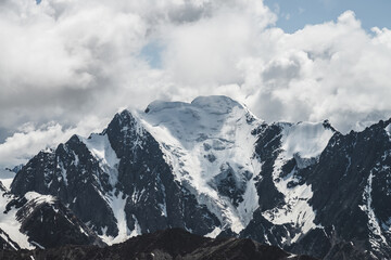 Fototapeta na wymiar Atmospheric minimalist alpine landscape with massive hanging glacier on big mountain under cloudy sky. Cracks on ice. Low clouds over snowbound huge mountain range. Majestic scenery on high altitude.