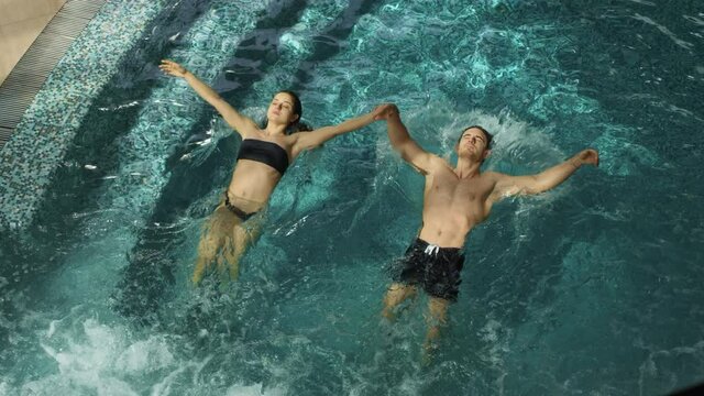 Couple jumping synchronously in pool. Man and woman submerging under water.