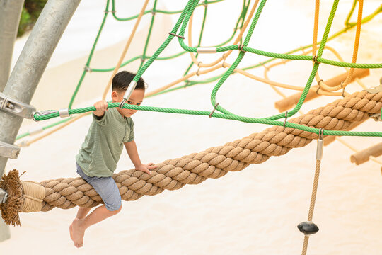 asia boy enjoying activity in a climbing adventure park on a summer day. Boy climbing ropes - Powered by Adobe