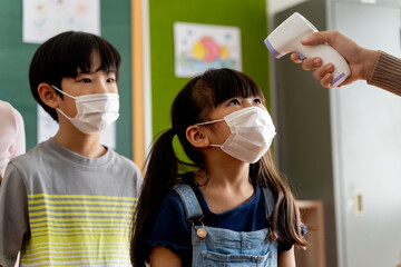 Group of Asian students in school building checked and scanned for temperature check. Elementary pupils are wearing a face mask and line up before entering into classroom. Covid-19 school reopen