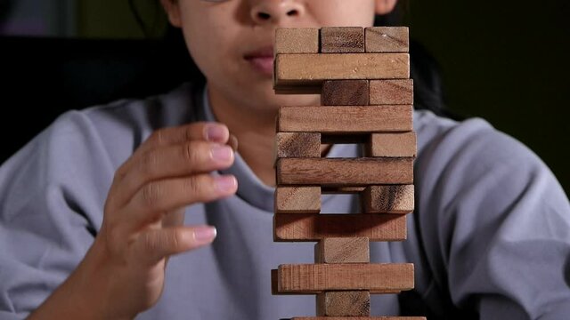 Woman thinking and concentrating on pulling out a wooden blocks in room alone. Jenga falls on the table. Concept of success and failure in the business.