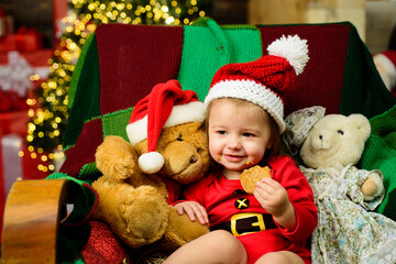 Cute baby face in Santa hat near Christmas tree. New year kids. Babyhood, childhood and people concept - happy baby in santa hat over holidays lights background.