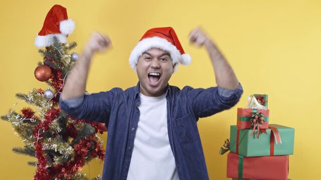 Young asian man celebrate merry christmas and happy new years with two hands steching in the air in yellow room.4K Resolution.