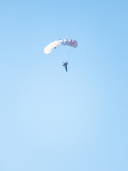 one parachutist floats slowly at low altitude on the background of clear sky