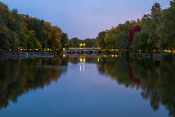Autumn landscape. Evening time, colorful trees, slowly river. Mirror water  and old stone bridge with lights . Guelph, Ontario, Canada