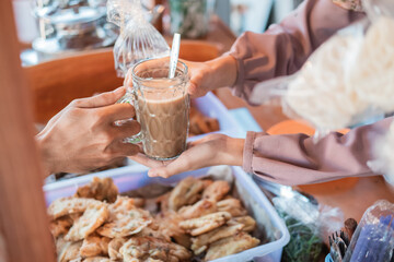 close up of a woman's stall waitress' hand holding a drinking glass, serving customers at the stall