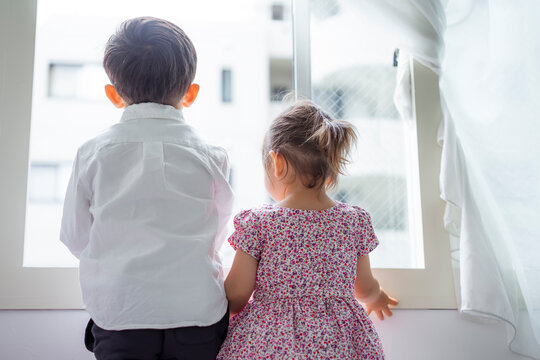 窓から外を眺める男の子と女の子の後ろ姿