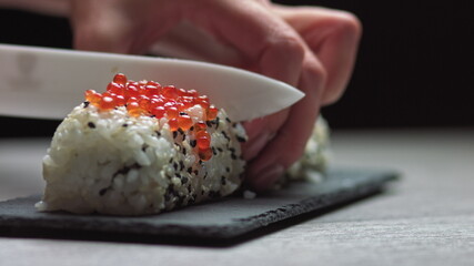 Chef cutting rolls of sushi with a knife on a stone board. - shot at a low angle. Beautiful female...