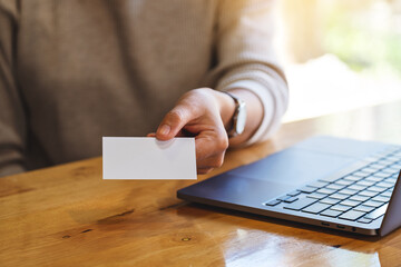 Closeup image of a woman holding and giving a blank business cards while using laptop computer