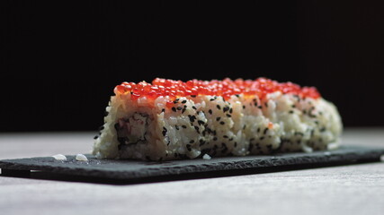 Sticks Take Sushi from Sushi box. Variety of types sushi with red caviar, fish, Philadelphia cheese and chopsticks close-up. Set of delicious Japanese sushi rolls.sushi on a stone board on a black