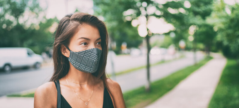 Asian woman walking outside wearing stylish fashion cloth face mask in plaid pattern. Serious young ethnic model portrait banner panorama.
