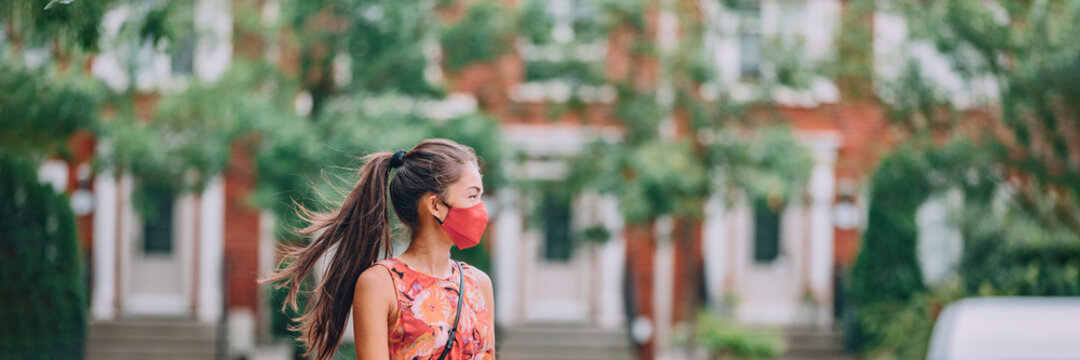 Asian woman walking in city street wearing mandatory protective face mask. Panoramic people lifestyle during coronavirus pandemic.