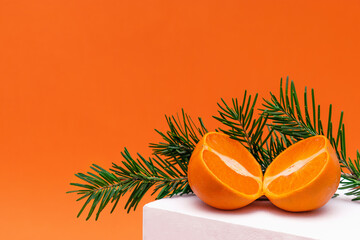 Fototapeta na wymiar Modern still life with tangerine cut in half and fir branches on white podium. New Year,Christmas and winter concept with food and geometric objects on orange background.Copy space for text