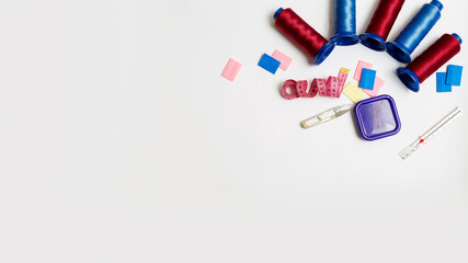 Sewing accessories: spools of thread, pins,chalks,tape and other sewing tools on a white background with copy space. Top view. Flat lay