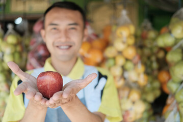 Fototapeta premium The shop assistant hands over the apples with two hands against the background of the smiling shop assistant