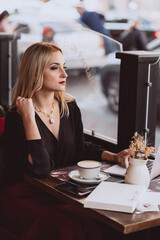 Beautiful young business woman enjoys a cup of coffee in a cafe during lunch break in autumn. Soft selective focus, artistic noise.