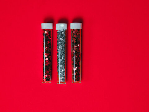Bottles of festive colored glitter on a red background.