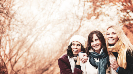 Three attractive happy women walking together in autumn park