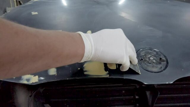 Man repairing damage on car in garage.Smearing putty on car dent on hood.Close up track shot.