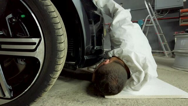 Repair man lying on ground and attaching new bumper on sport car in service station.Low angle close up.