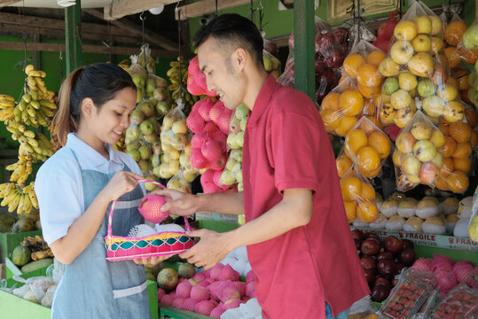 A smiling female shopkeeper in apron give service for male customers who want to buy fruit parcels in the fruit market