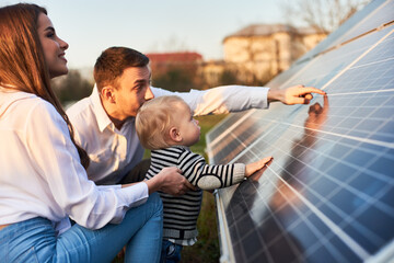 Side close-up shot of a young modern family with a little son getting acquainted with solar panel...