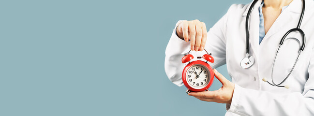 Doctors hands holding red alarm clock over blue background. Time is crucial life saver. Medical...