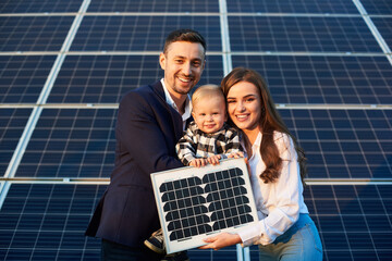 Portrait of a young family holding a small solar panel and a baby boy, smiling and looking at...